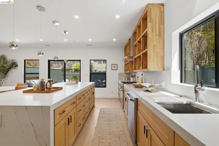 Spacious kitchen featuring a large central island with light wood cabinetry and a light-toned countertop, complemented by a perimeter counter with an undermount sink and stainless steel appliances