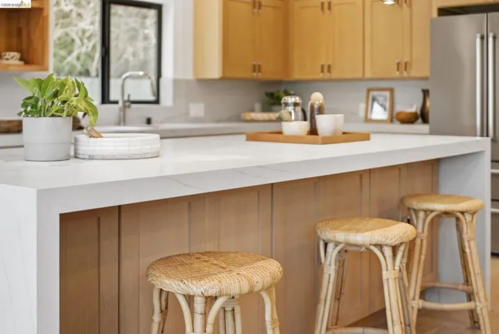 Kitchen island with a waterfall countertop, integrated sink, and light wood cabinetry