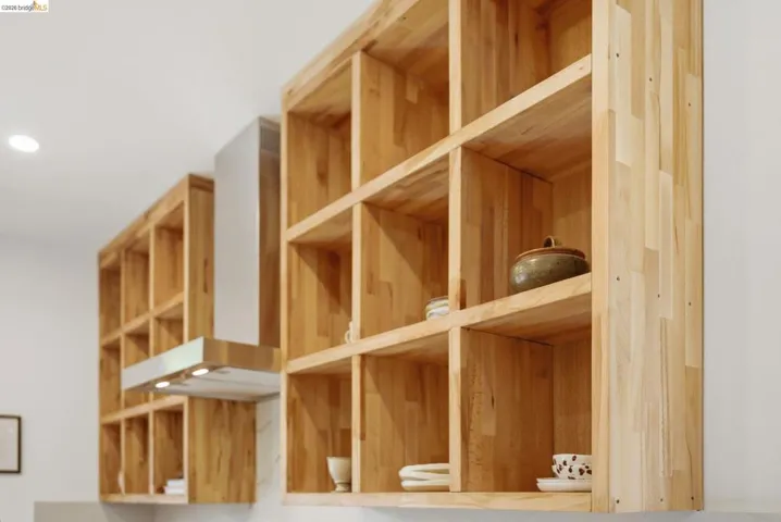 Custom wood shelving with open cubbies, integrated stainless steel range hood, recessed ceiling lighting, and light-toned countertops