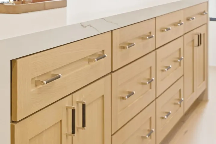 Light wood-finish cabinetry with polished chrome hardware and a white countertop featuring subtle veining