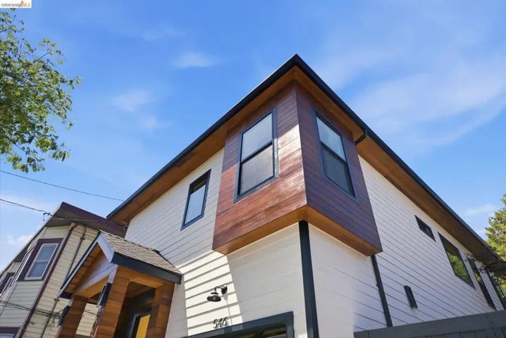 Contemporary exterior showcasing a wood-look accent bay window, light-colored horizontal siding, dark trim details, a covered entry with wood-look siding, and a dark pitched roof