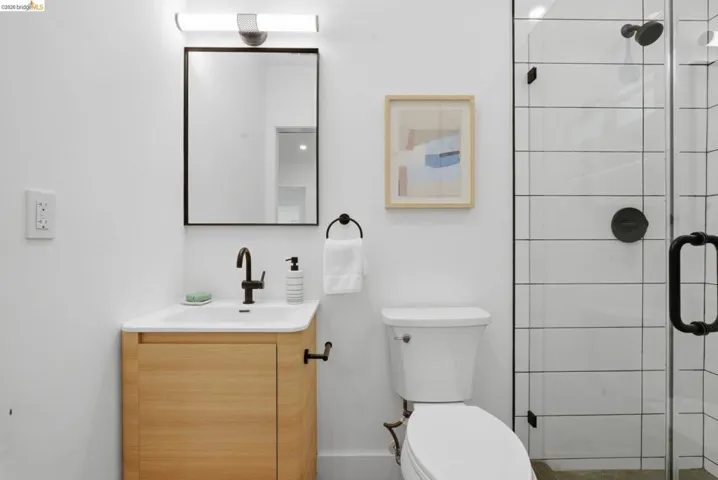 Bathroom featuring a light wood-finish vanity, matte black fixtures, a contemporary mirror, and a glass-enclosed shower with subway tile