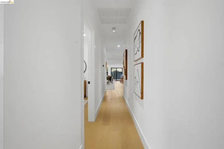 Long hallway featuring light wood-finish flooring, white walls, and recessed lighting