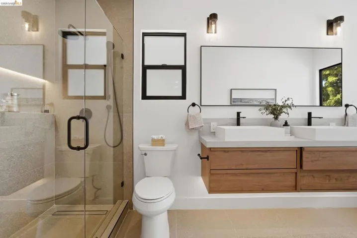 Spacious bathroom featuring a frameless glass shower enclosure, a dual-sink floating vanity with wood-finish cabinetry, a large framed mirror, and contemporary sconce lighting