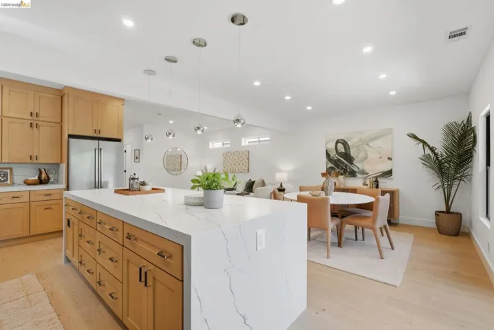 Open-concept kitchen and dining area featuring a waterfall island with a stone countertop, wood-finish cabinetry, stainless steel appliances, recessed lighting, and wood-finish flooring