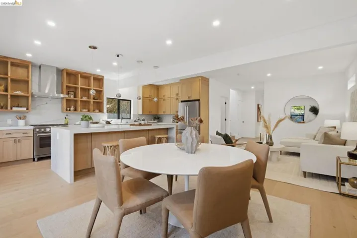 Open-concept living space featuring wood-finish flooring, recessed lighting, and a kitchen with light wood cabinetry, a stainless steel range with a ventilation hood, and an island with a white countertop