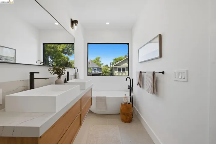 Contemporary bathroom featuring a floating wood-finish double vanity with rectangular vessel sinks, matte black faucets, and a freestanding soaking tub
