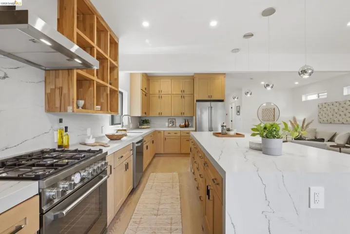 Gourmet kitchen featuring a stainless steel range with overhead hood, wood-finish cabinetry, a large center island with pendant lighting, and white countertops with a matching backsplash