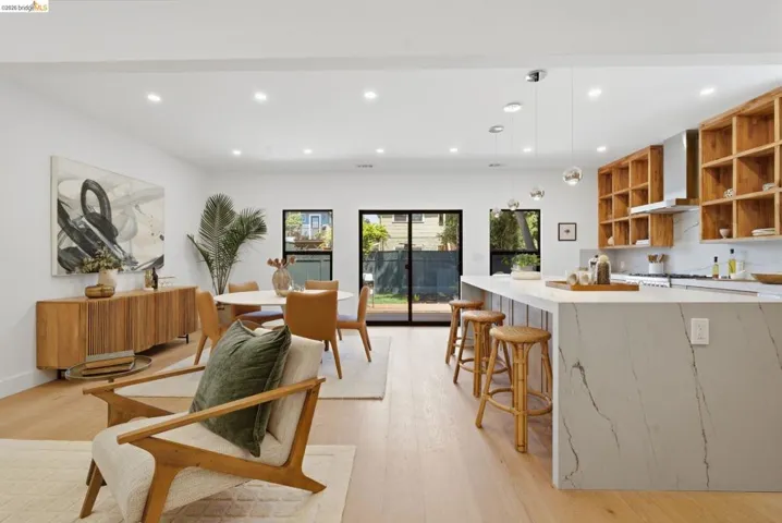 Spacious open-concept living area featuring a kitchen island with stone waterfall countertop, wood-finish flooring, recessed lighting, and sliding glass doors