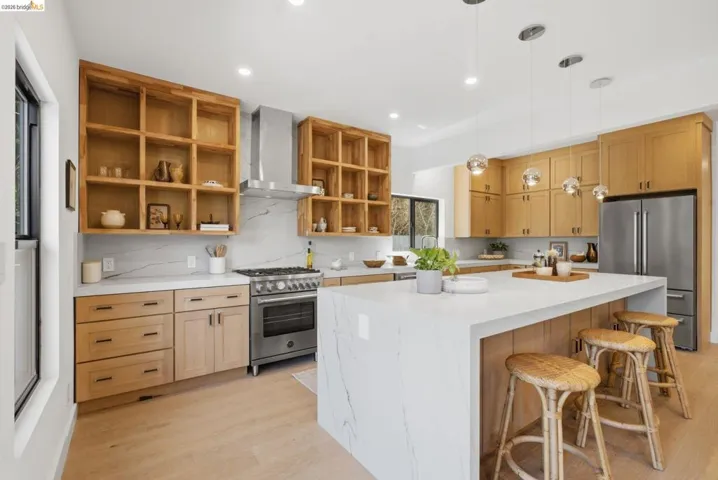 Contemporary kitchen featuring light wood cabinetry, white countertops with veining, stainless steel appliances, a large island with seating, and recessed lighting