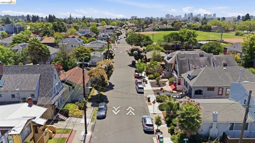 Street-level view of a residential area featuring multiple single-family homes, mature trees, and a distant city skyline