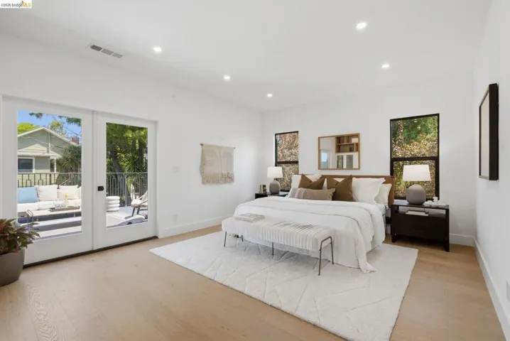 Bright bedroom featuring a private balcony with black wrought iron railings, light wood-finish flooring, recessed lighting, and large windows