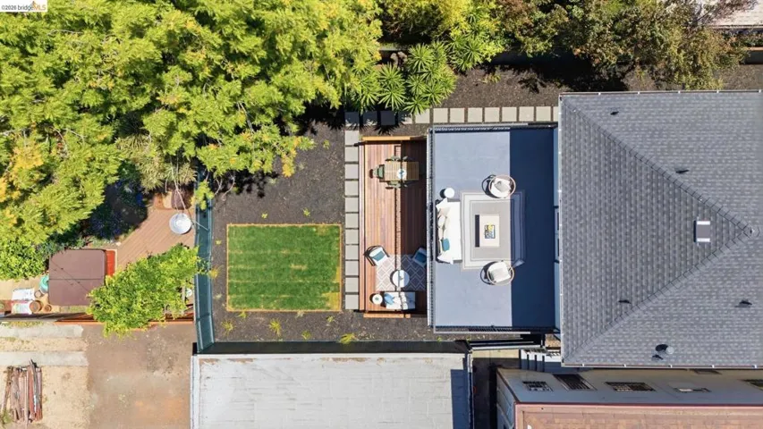 Expansive outdoor living area featuring a large rooftop deck, a wooden patio, a manicured lawn area, mature trees, and a hot tub