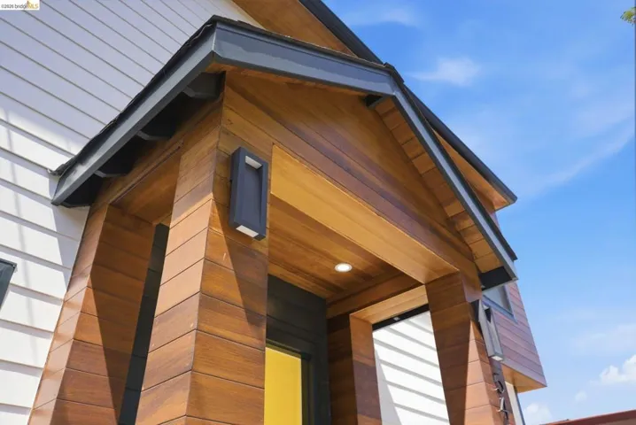 Architectural facade featuring horizontal white siding, wood-finish paneling, dark trim, and modern exterior lighting fixtures