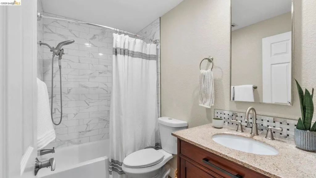 Bathroom featuring a shower-tub combination with subway tile surround, a built-in vanity with a speckled countertop, an oval undermount sink, and a mirrored medicine cabinet