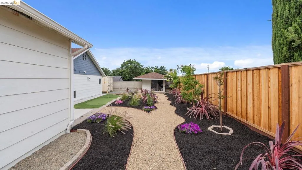 Landscaped backyard featuring a meandering gravel pathway, rich dark mulch beds with vibrant plantings, a putting green, and a privacy fence