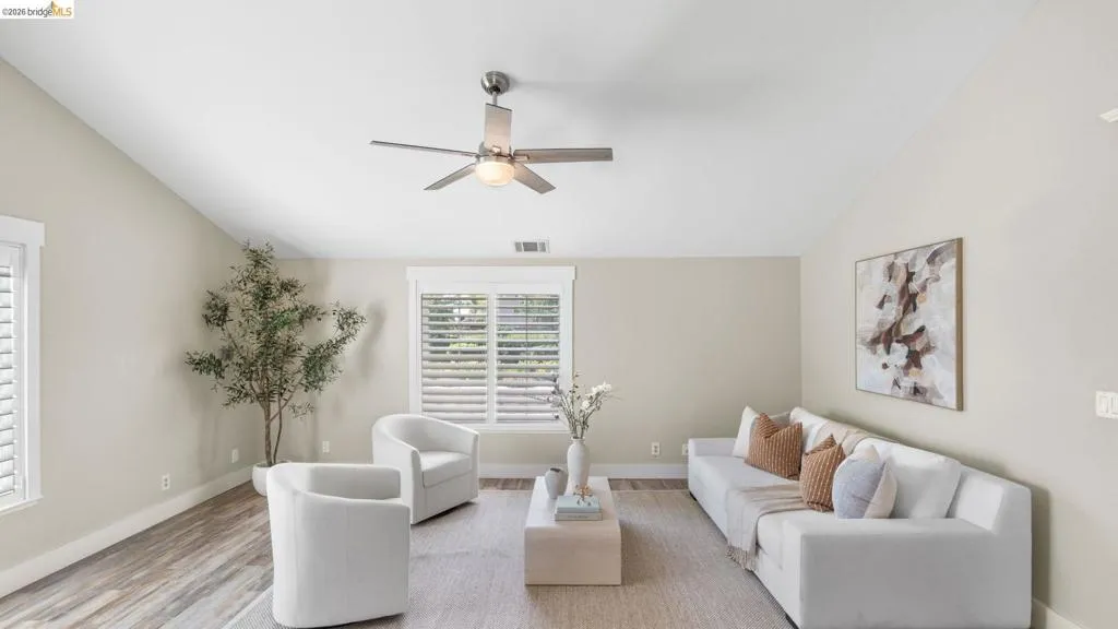 Vaulted ceiling living area featuring wood-finish flooring, a contemporary ceiling fan, and multiple windows with plantation shutters