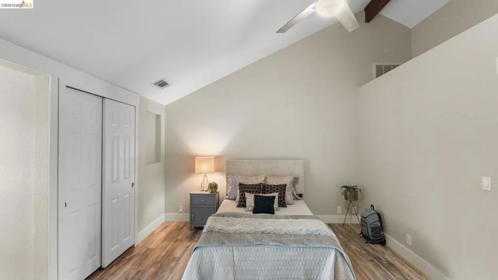 Bedroom featuring vaulted ceilings with exposed wood beams, wood-finish flooring, a ceiling fan, and a bi-fold closet