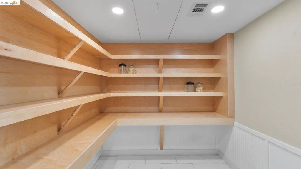 Expansive pantry featuring light wood-finish shelving, an integrated countertop workspace, white wainscoting, and recessed ceiling lighting