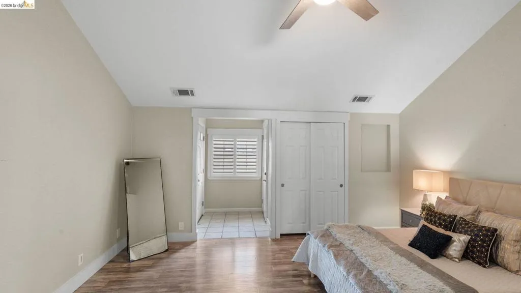 Spacious room featuring wood-finish flooring, light neutral wall paint, and a vaulted ceiling with a ceiling fan