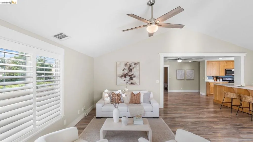 Vaulted ceilings enhance this living area featuring wood-finish flooring, plantation shutters, and a contemporary ceiling fan