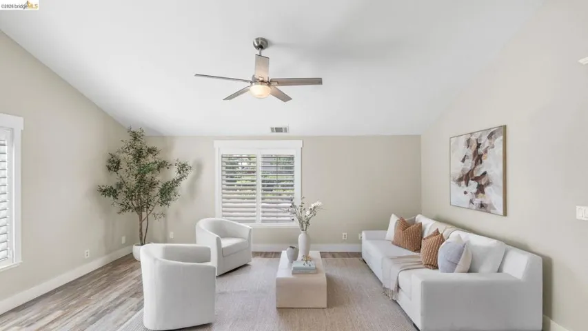 Vaulted ceiling living area featuring wood-finish flooring, a contemporary ceiling fan, and multiple windows with plantation shutters