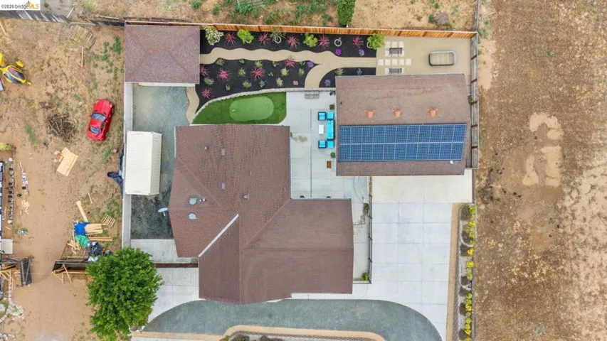 Expansive aerial view showcasing a multi-gabled roofline, solar panel array, paved driveway, dedicated putting green, and landscaped garden beds with decorative rock