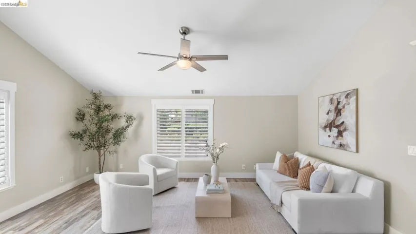 Vaulted ceiling living area featuring wood-finish flooring, a contemporary ceiling fan, and multiple windows with plantation shutters