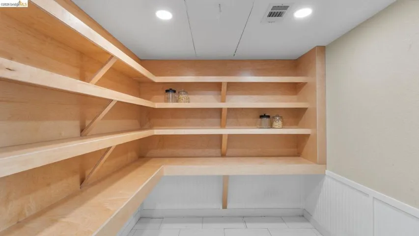 Expansive pantry featuring light wood-finish shelving, an integrated countertop workspace, white wainscoting, and recessed ceiling lighting