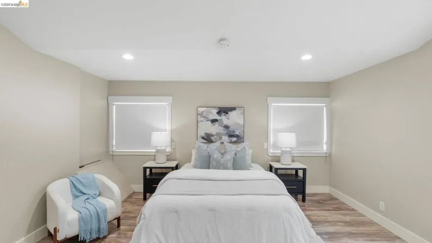 Bedroom featuring wood-finish flooring, recessed lighting, neutral wall tones, and two windows with roller shades