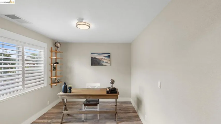 Room featuring wood-finish flooring, a contemporary flush-mount ceiling light fixture, and a window with white plantation shutters