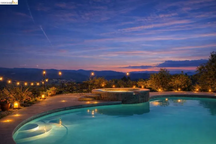 Pool at dusk with a mountain view and a pool with connected hot tub - AI staged. See following photos for original.
