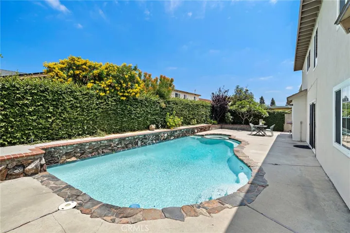 Double French sliders lead from the family room to a wonderfully private backyard oasis designed for entertaining and relaxation, featuring a sparkling pool and spa edged in flagstone, raised flagstone planters, and an expansive deck area perfect for gatherings