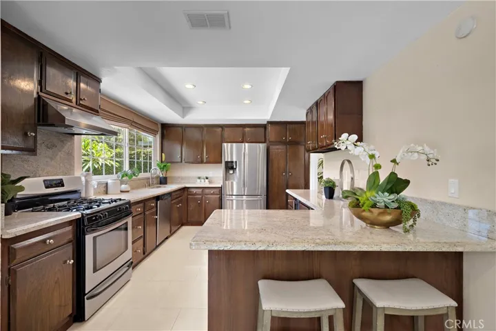 complete with granite countertops, rich dark wood cabinetry, a breakfast bar, stainless sinks, stainless appliances including a gas stove, vent hood, dishwasher, and wine refrigerator, plus an inside laundry room conveniently located off the kitchen.