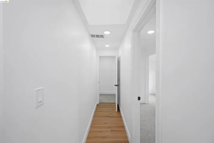 Interior hallway featuring wood-finish flooring, white walls, recessed ceiling lighting, and multiple doorways