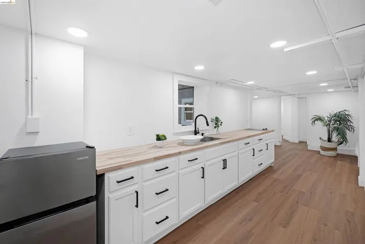 Extended kitchen area featuring wood-finish countertops, white cabinetry with matte black hardware, and a single basin sink with a black gooseneck faucet