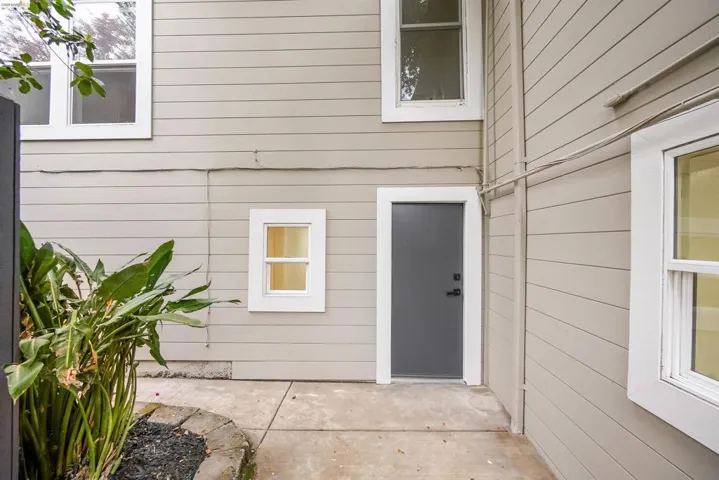 Exterior siding in a light neutral tone featuring white window trim, a contemporary grey door, and concrete hardscaping