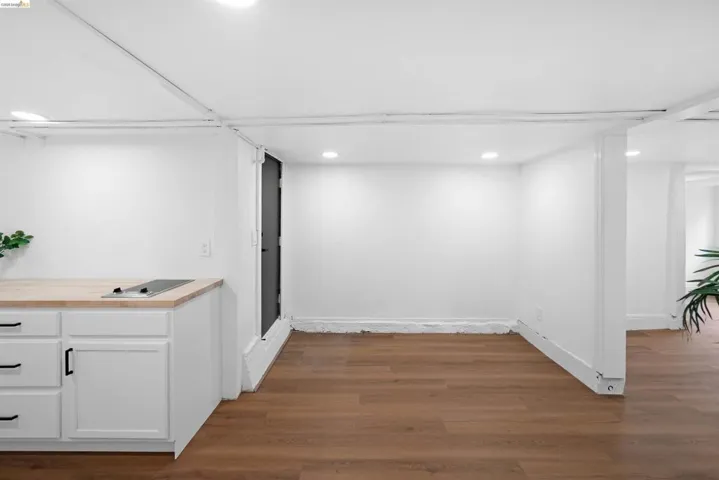 Compact kitchen area featuring white cabinetry with black hardware, a light wood-finish countertop, and an integrated cooktop
