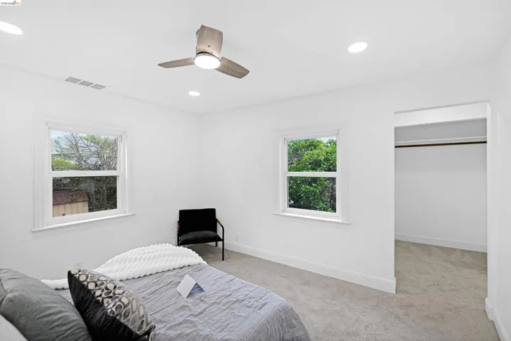 Room featuring light gray carpeting, two double-hung windows with white trim, and a contemporary ceiling fan with integrated lighting