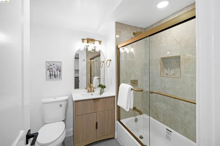 Bathroom featuring a shower-tub combination with gold-finish sliding glass doors, a built-in shower niche with hexagonal tile, and large format wall tiling