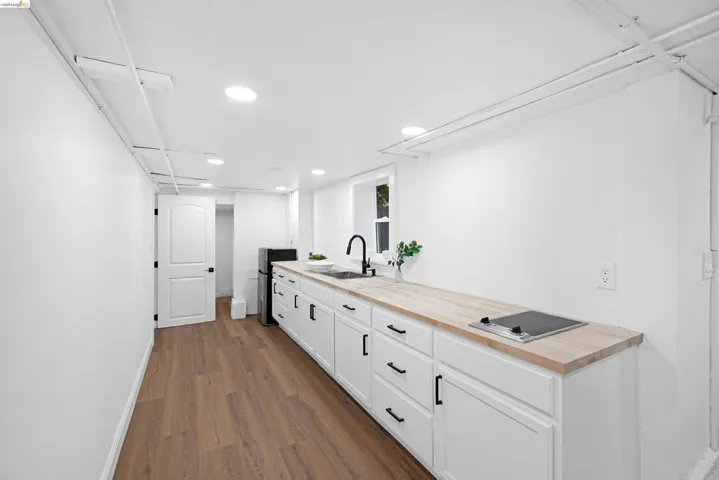 Kitchenette featuring light wood-finish countertops, white cabinetry with black hardware, and an integrated two-burner cooktop