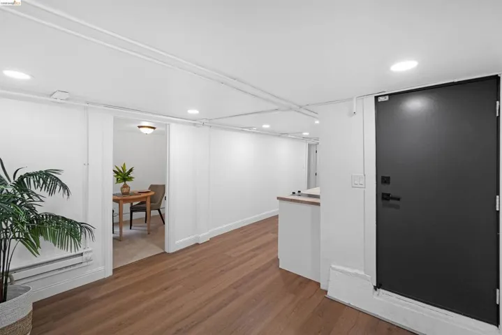 Interior hallway featuring wood-finish flooring, recessed lighting, white walls, and a black solid door with contemporary hardware