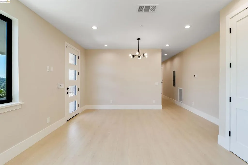Spacious room with light wood-finish flooring, recessed lighting, and a contemporary chandelier