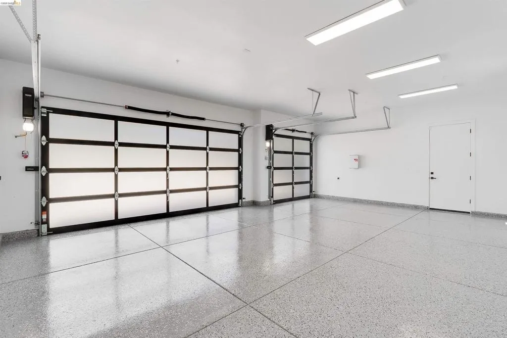 Spacious garage featuring two modern glass-panel garage doors, a polished epoxy floor finish, and multiple overhead linear light fixtures