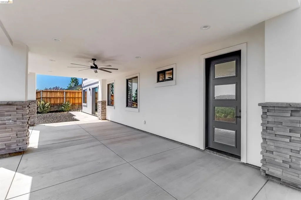 Covered patio featuring a concrete slab, stone veneer pillars, and a ceiling fan