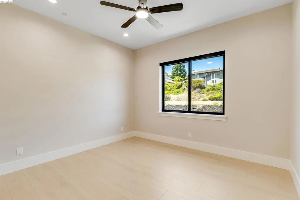 Spacious room featuring light wood-finish flooring, recessed lighting, a ceiling fan, and large black-framed windows