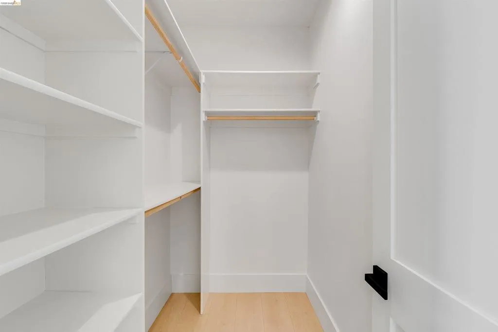 White built-in closet system with multiple shelving units, light wood-finish flooring, and a contemporary black door handle