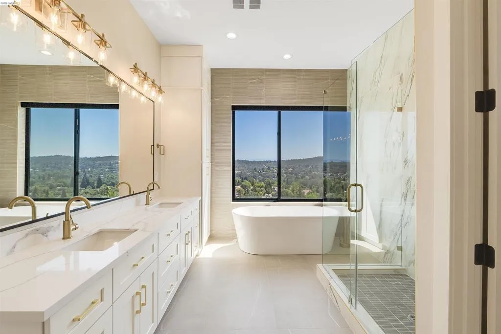 Bathroom featuring a freestanding soaking tub, a frameless glass-enclosed shower, a dual vanity with a white countertop, gold-finish fixtures, and large format tile flooring