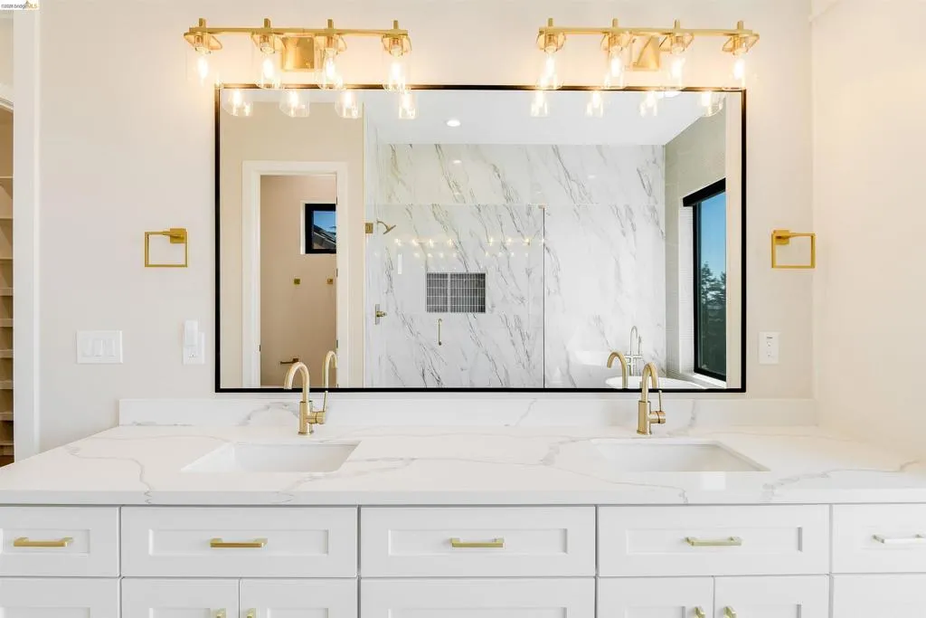 Dual vanity with white cabinetry, gold-finish hardware, and a stone countertop