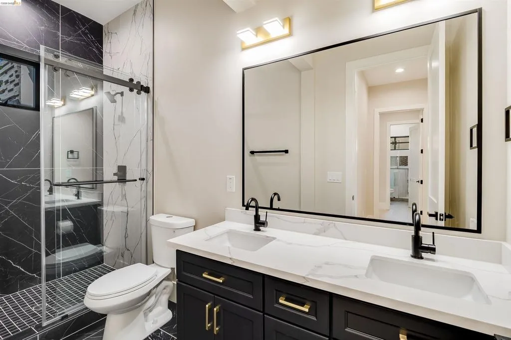 Bathroom featuring a dual vanity with white countertops and undermount sinks, matte black cabinetry with gold hardware, and a frameless mirror with a black border